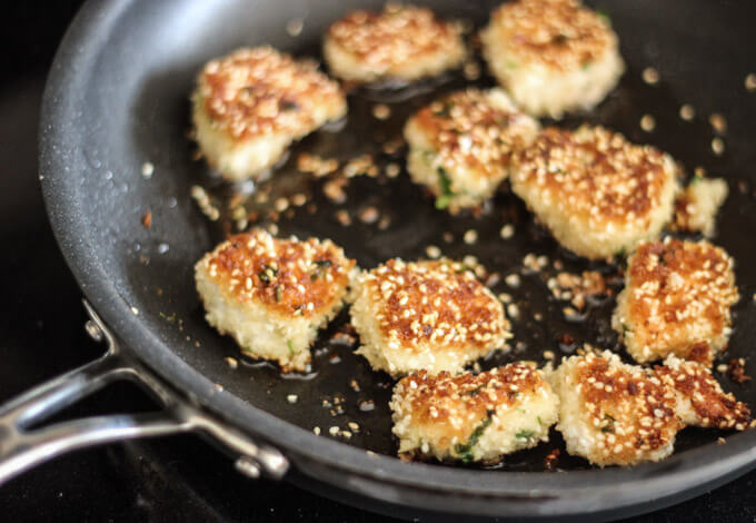 chicken pieces in a skillet coated with sesame seeds.