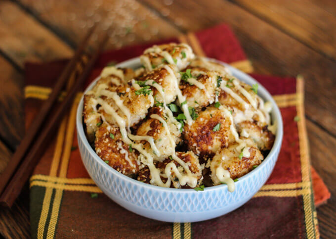 crispy chicken bites drizzled with sauce and garnished with chopped cilantro in a bowl.