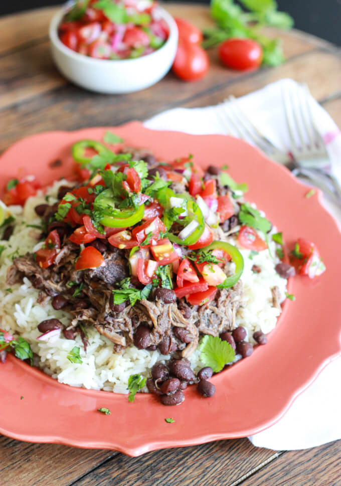 shredded pork and beans over rice with fresh tomato salsa on top in a red plate.