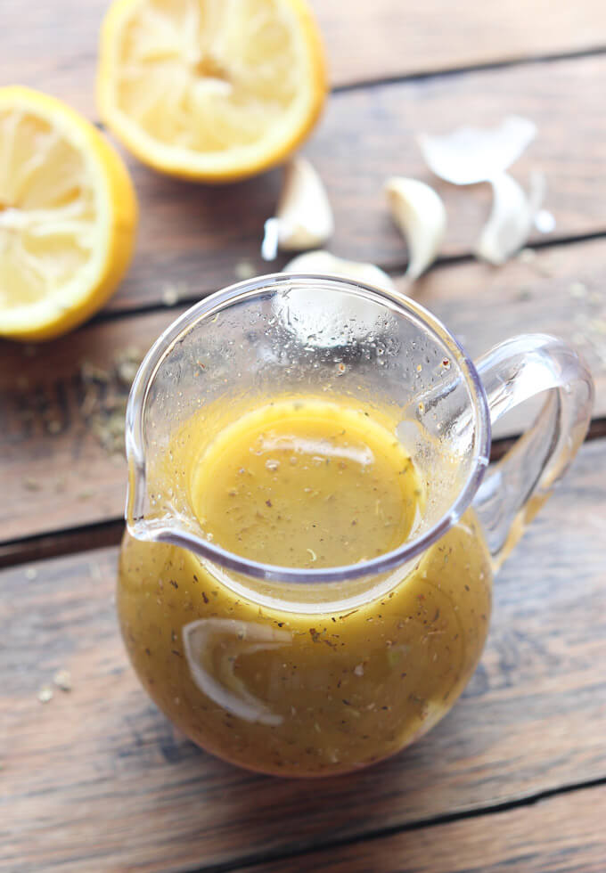 Overhead of greek salad dressing recipe with lemon and garlic in background.