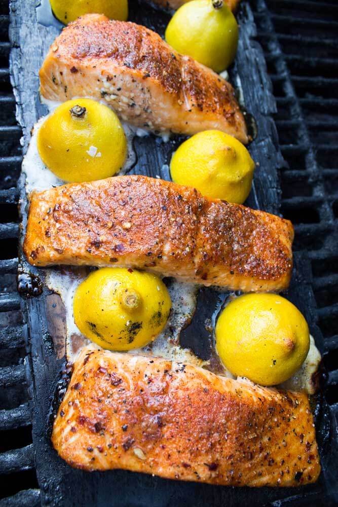 grilled salmon on a cedar plank with halved lemons.