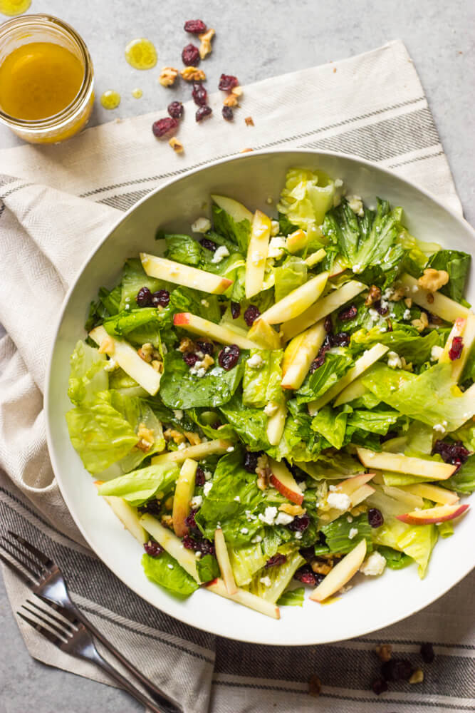 romaine salad with apples, walnuts, cranberry, and feta cheese in a white bowl.