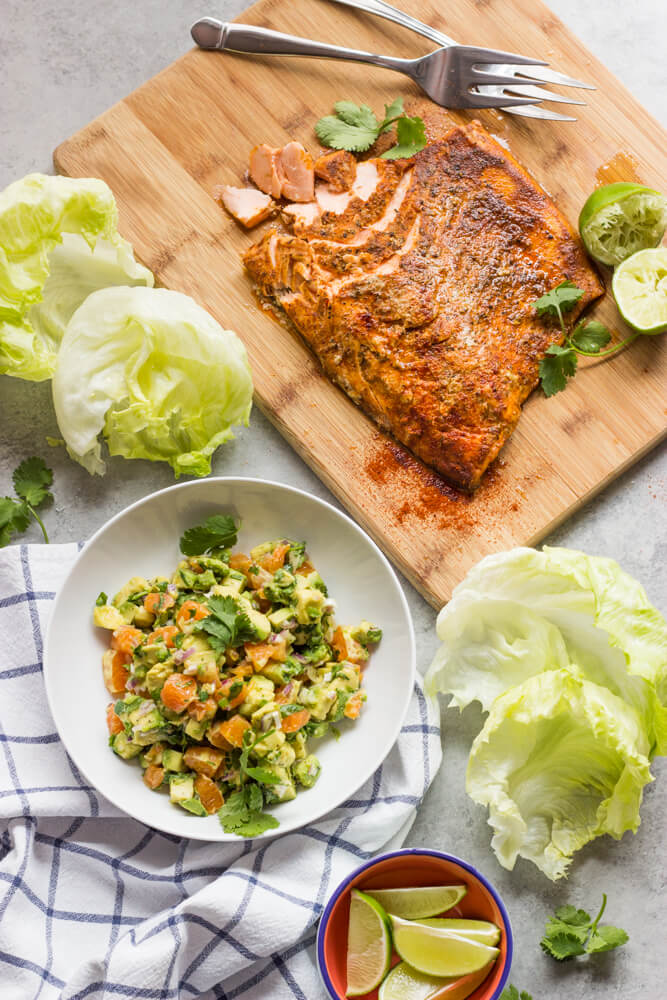 baked salmon a wooden board with a side of orange salmon and iceberg lettuce leaves.