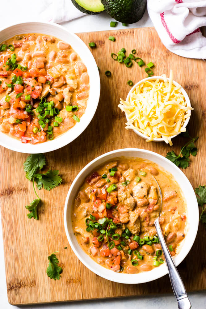 Overhead view of creamy chicken chili in white bowls with side of shredded cheese