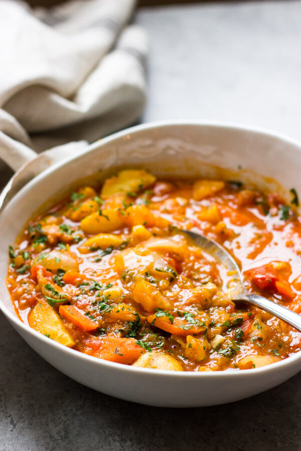 Side view of chicken stew with butternut squash in white bowl with a spoon on the side.