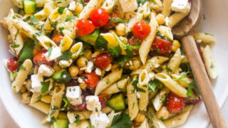 Cold pasta salad with italian dressing in white bowl and wooden spoon