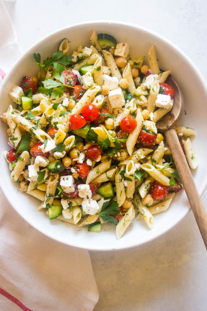 Cold pasta salad with italian dressing in white bowl and wooden spoon