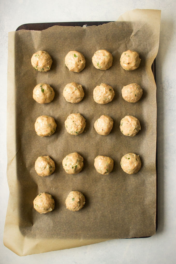 Raw chicken meatballs on parchment lined baking sheet