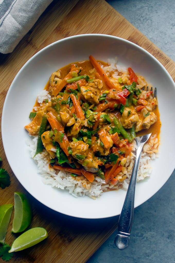 Chicken vegetable curry over white rice in white bowl with side of fork