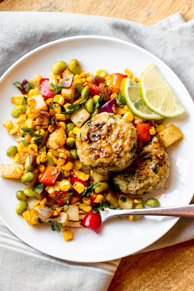 Chicken patties over corn succotash on a white plate