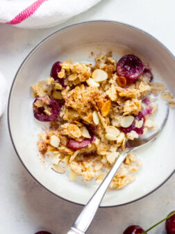 Oatmeal in white bowl with milk and cherries.