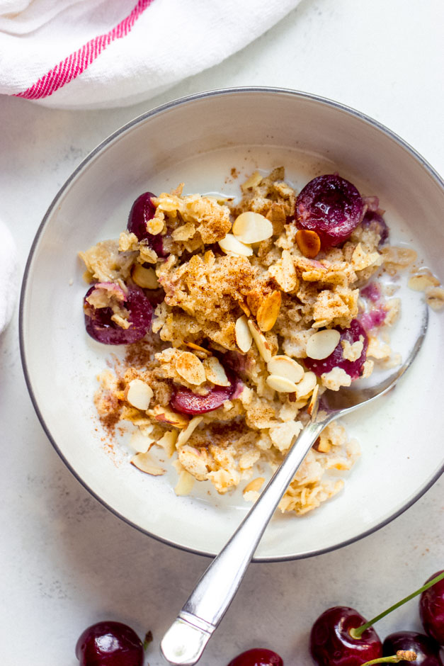 Oatmeal in white bowl with milk and cherries.