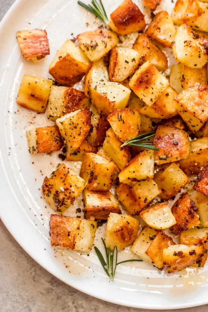 close up roasted garlic and rosemary potatoes garnished with fresh rosemary.