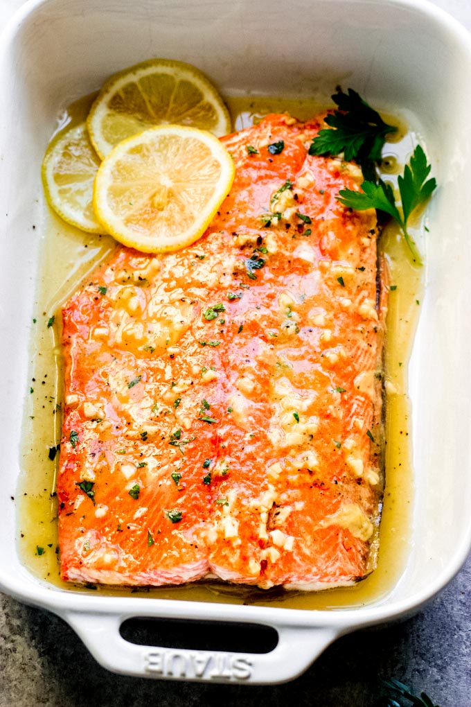 maple mustard salmon in a baking dish with sliced lemons and fresh parsley.