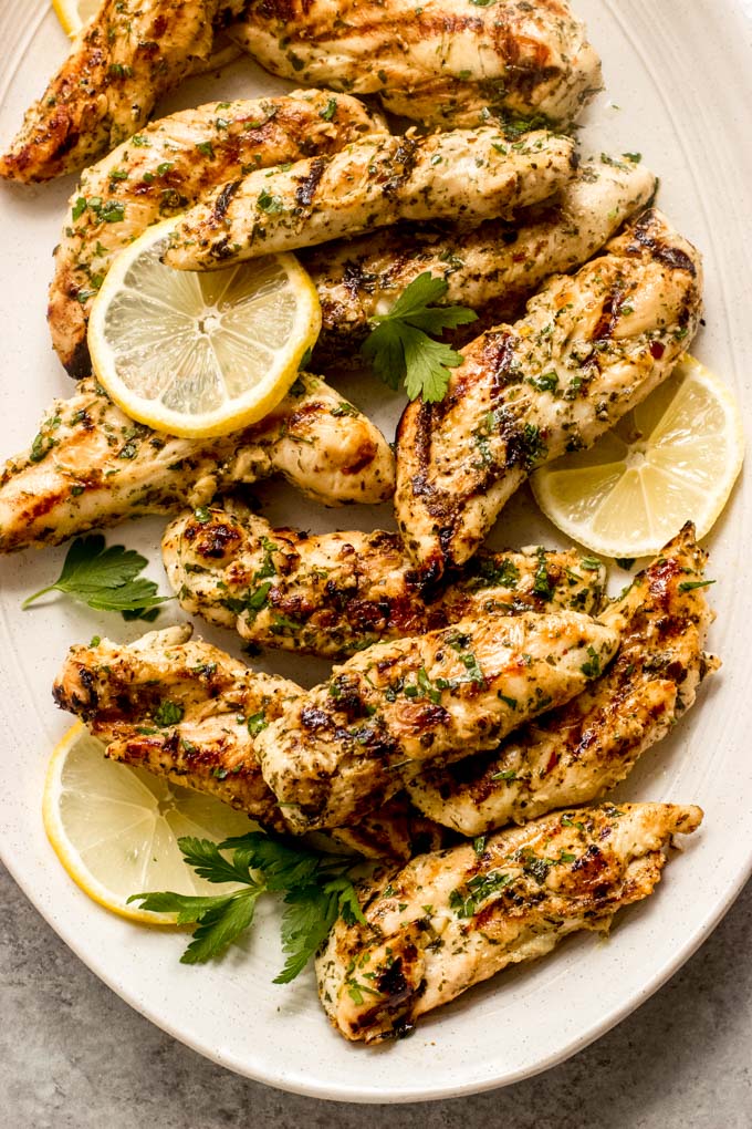 close up of easy grilled chicken tenders on a platter with sliced lemon.