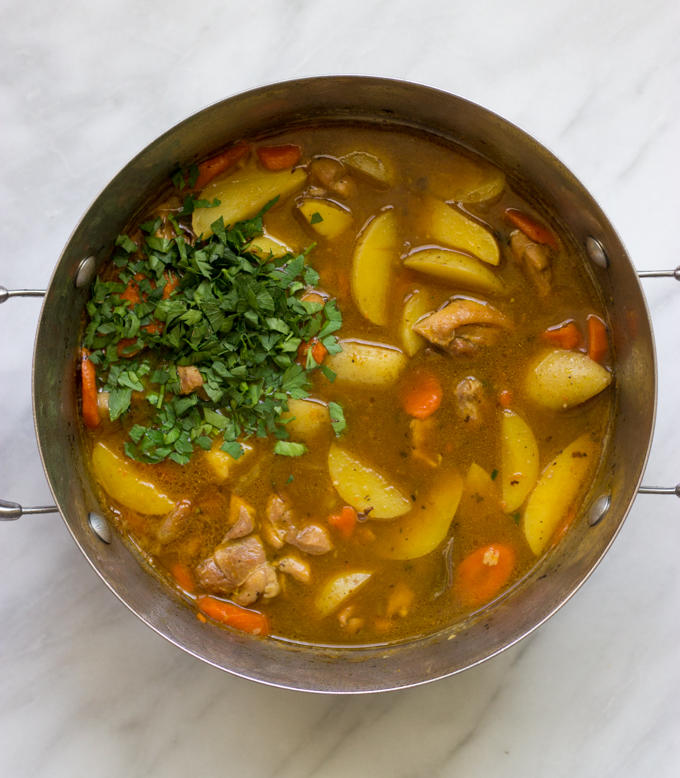 dutch oven with cooked chicken stew garnished with fresh parsley.