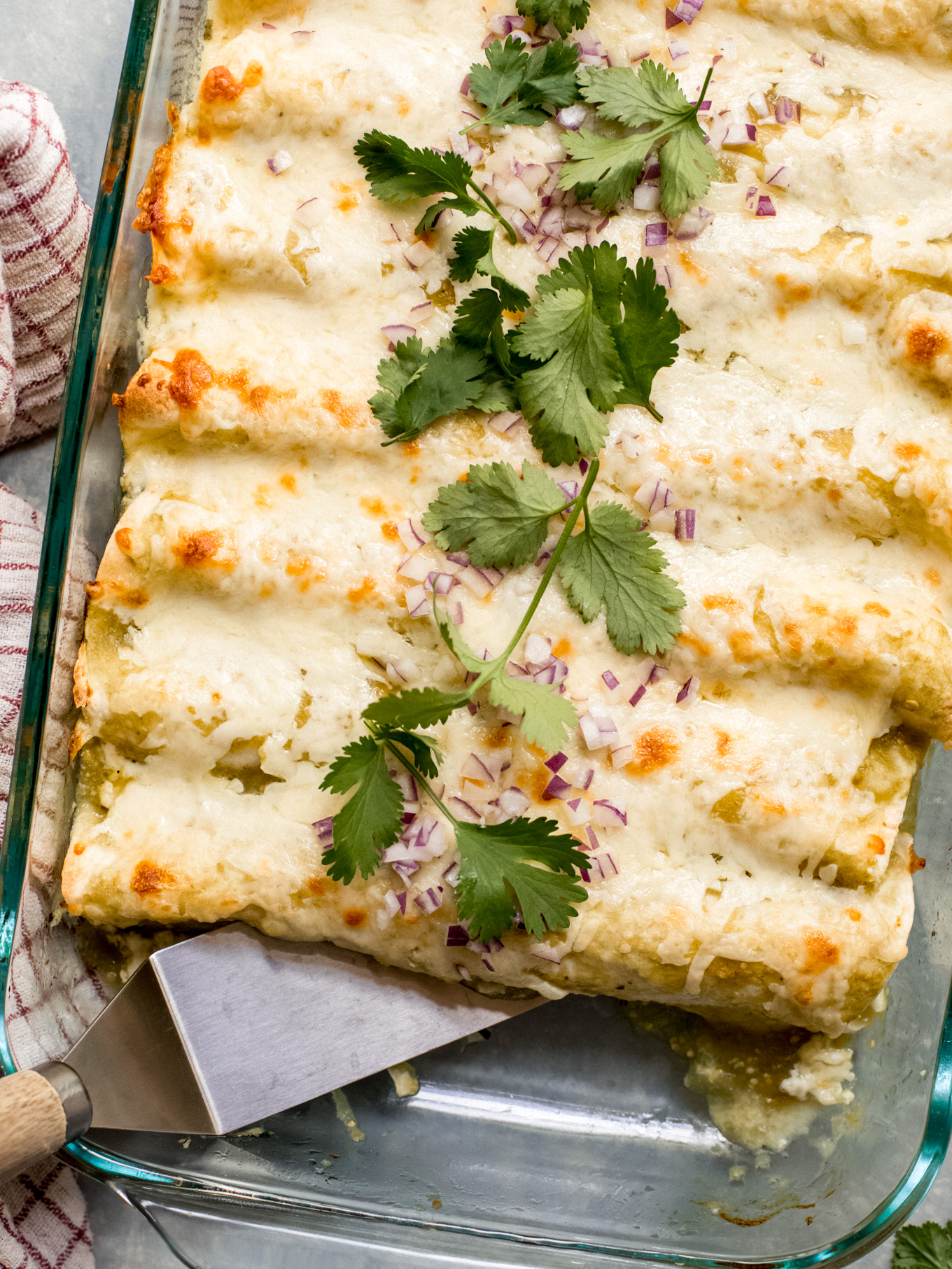 rolled up enchiladas verdes in glass baking dish with spatula on the side.