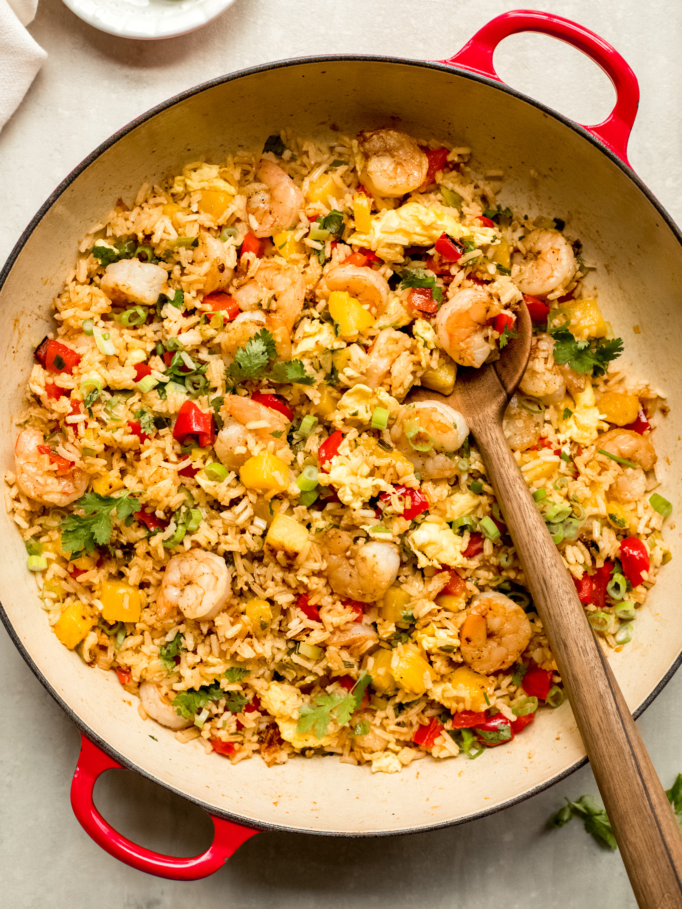 pineapple shrimp fried rice in a skillet with a wooden spoon lifting some out of the skillet.