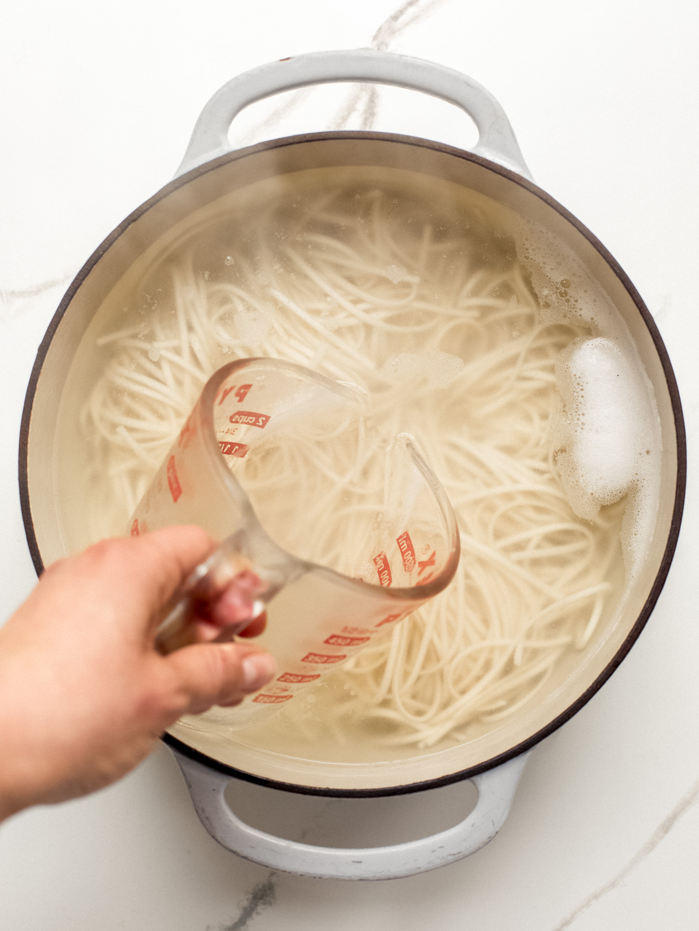 pasta in a pot with reserve pasta water in a measuring cup on the side.