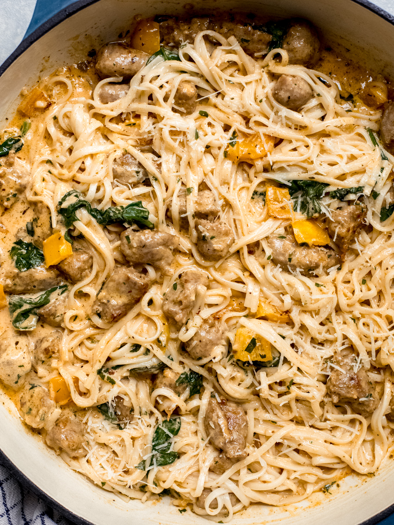 close up of creamy pasta with cream sausage, Italian sausage, bell peppers, and spinach in a skillet.