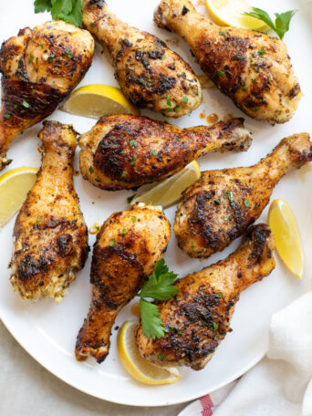 grilled chicken drumsticks on a white platter garnished with parsley and lemons.