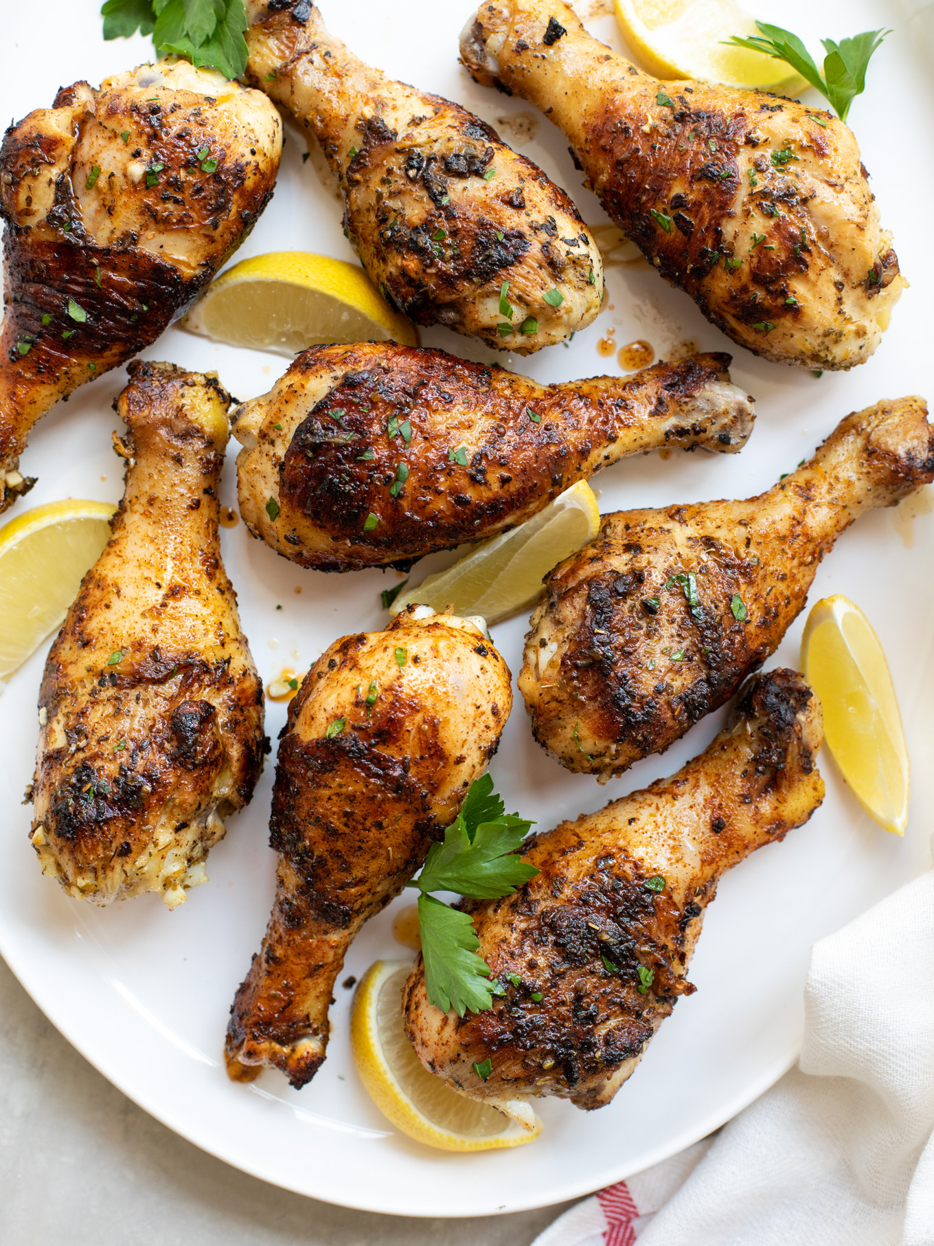 grilled chicken drumsticks on a white platter garnished with parsley and lemons. 