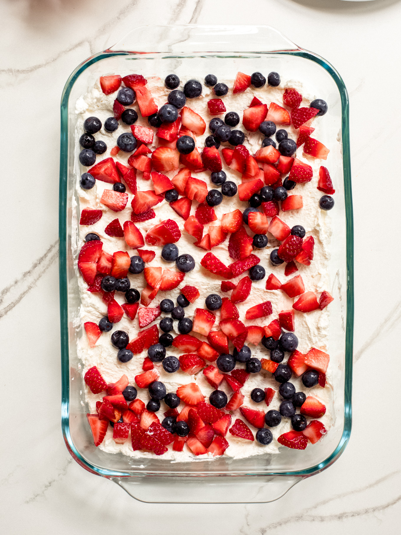 Layered cream and chopped up fruit in a glass baking dish.