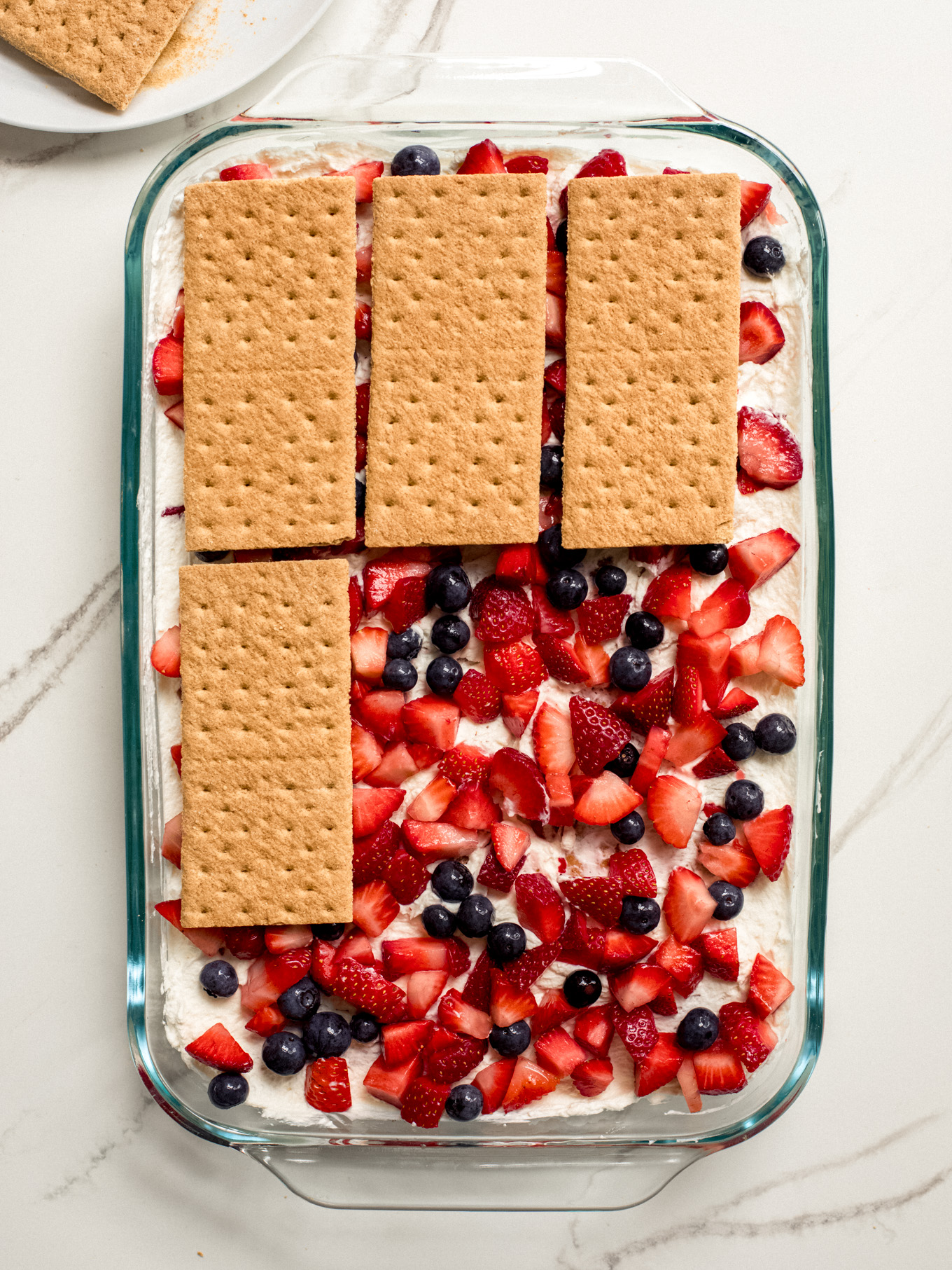 layered graham crackers over chopped fruit in a glass dish.