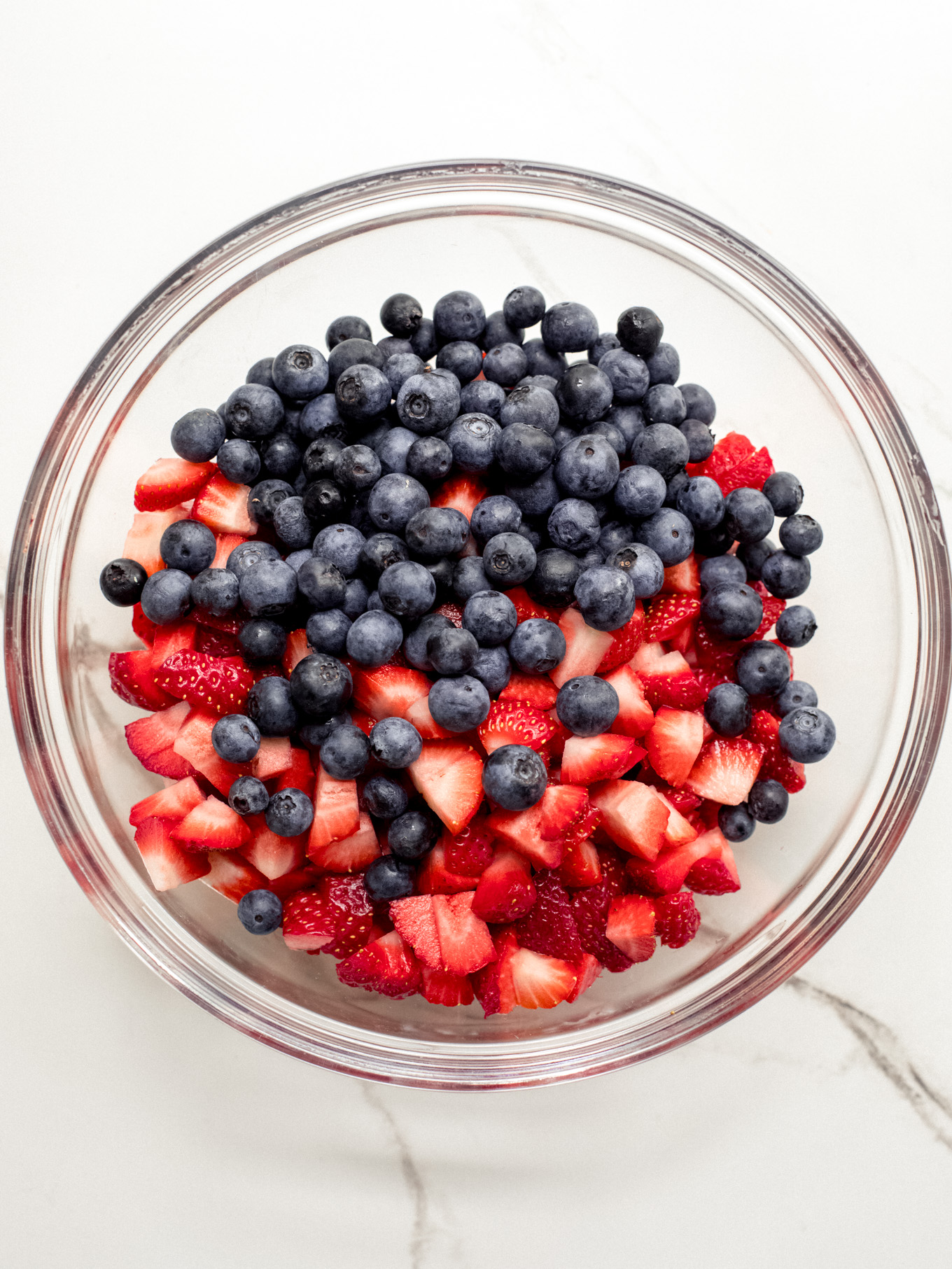 chopped up strawberries and blueberries in a glass bowl.