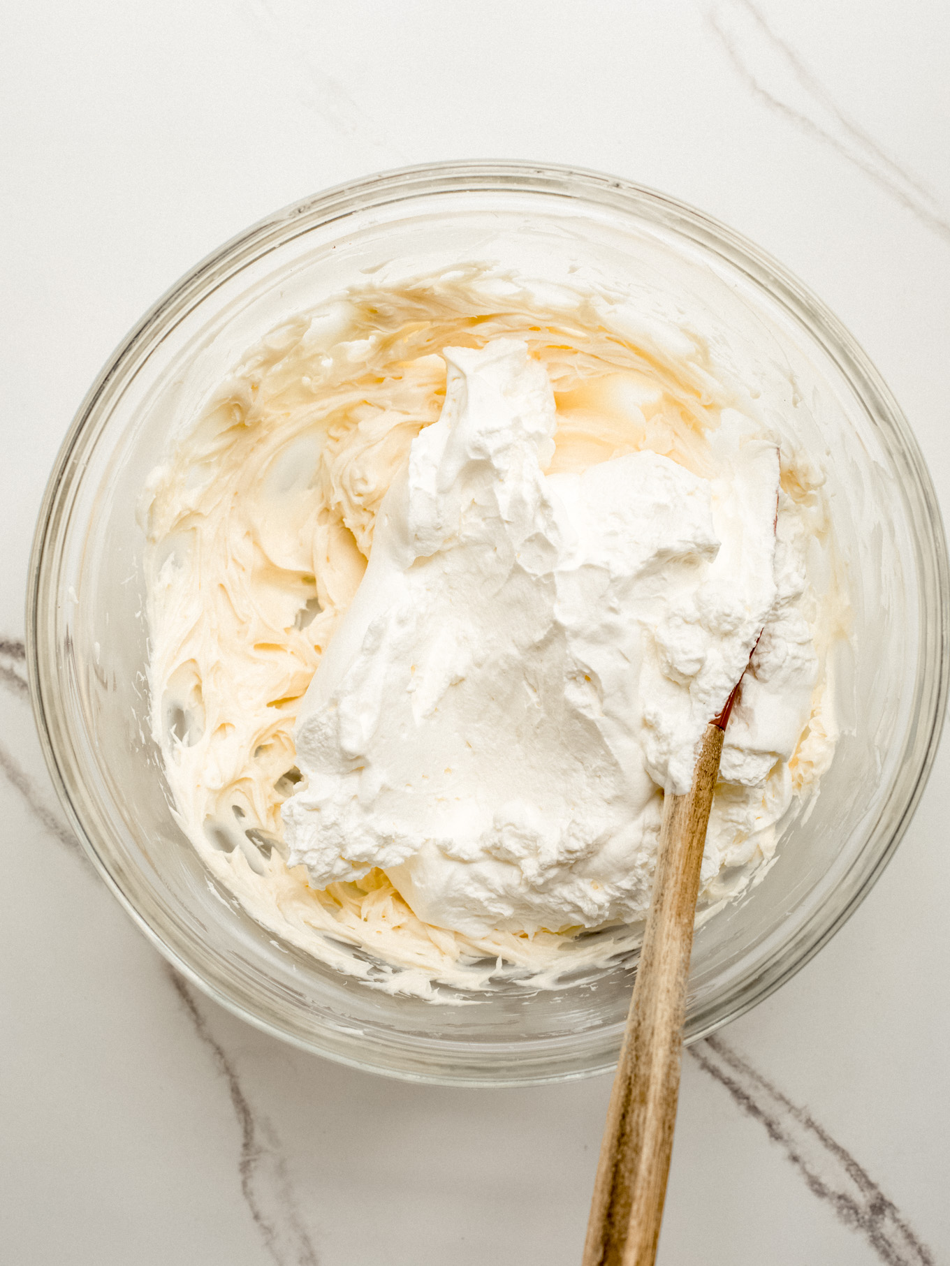 cream cheese mixture and whipped cream with rubber spatula in a glass bolw.