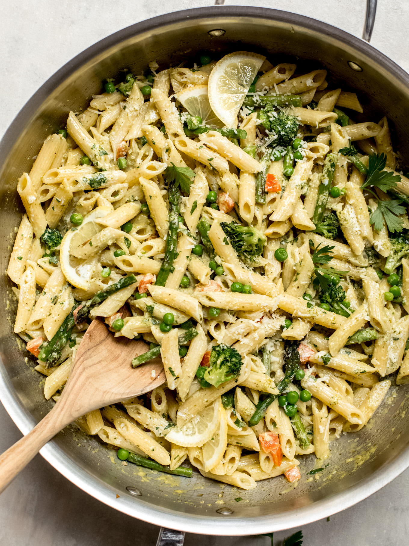 penne primavera in a skillet with a wooden spoon on the side.