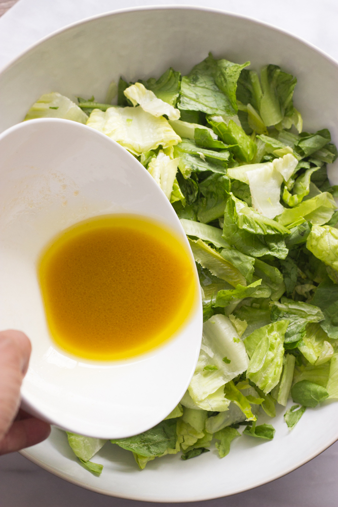 romaine lettuce in a bowl with salad vinaigrette being poured.