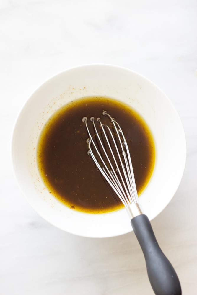 whisked balsamic dressing in a white bowl with a whisk.