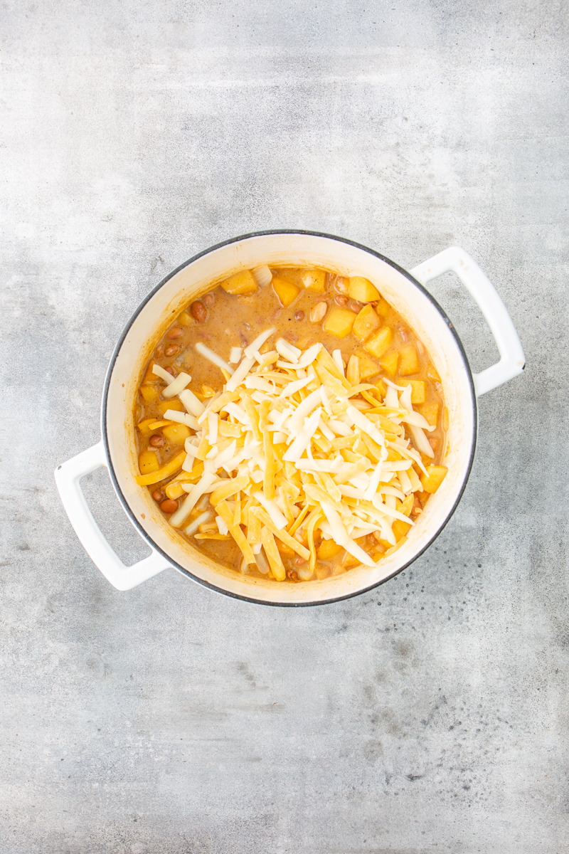 dutch oven with cooked chicken chili with apples and shredded cheese over the top.