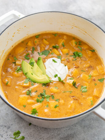 white dutch oven with apple chicken chili garnished with cilantro, sour cream, and sliced avocado.