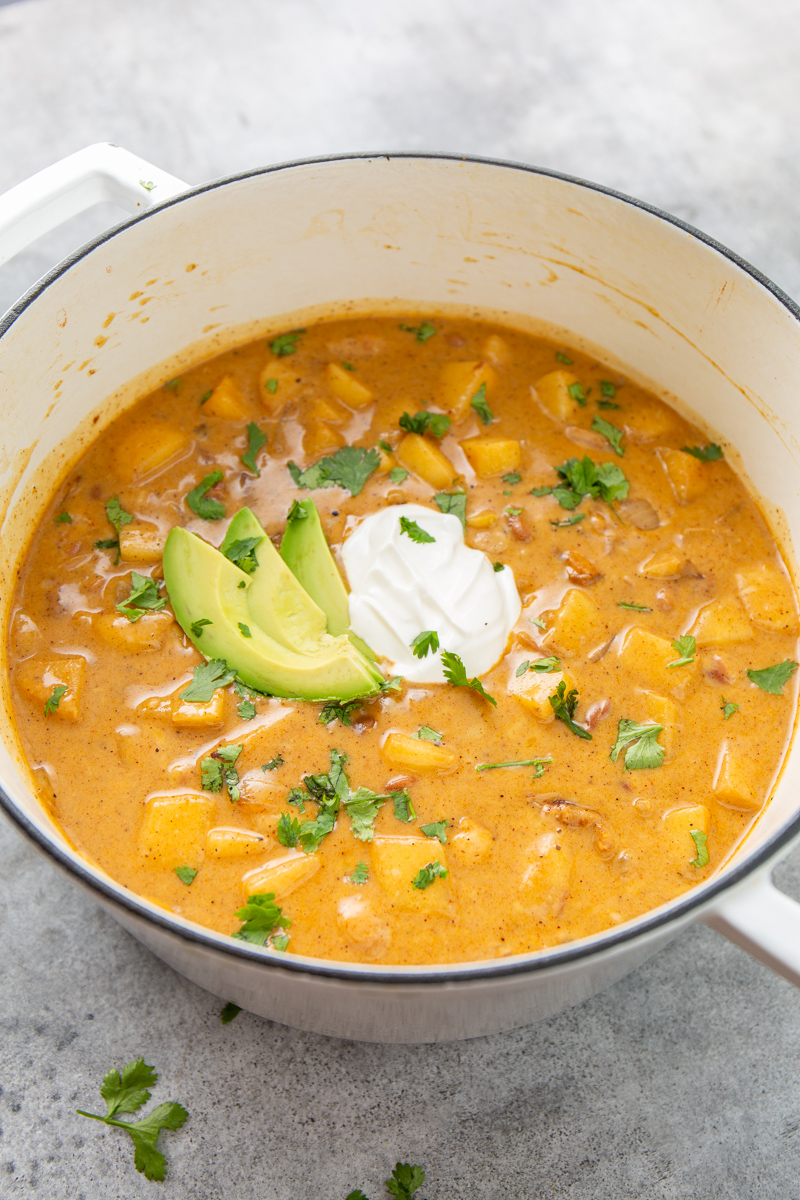 white dutch oven with apple chicken chili garnished with cilantro, sour cream, and sliced avocado.