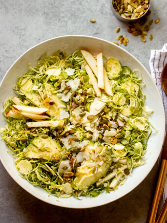 shredded Brussels sprouts salad in a white bowl with wooden utensils on the side.