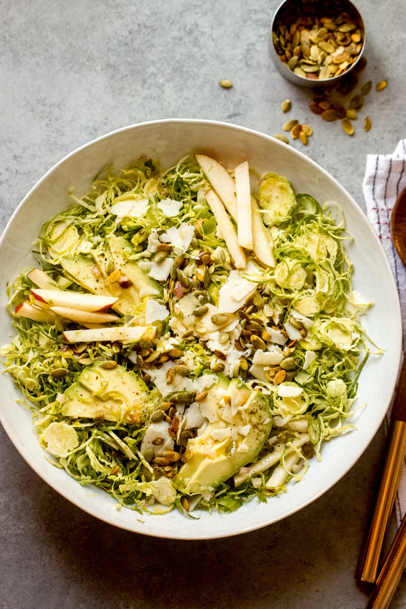 shredded Brussels sprouts salad in a white bowl with wooden utensils on the side.