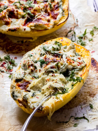 Baked spaghetti squash stuffed with artichoke spinach mixture with a fork on the side.