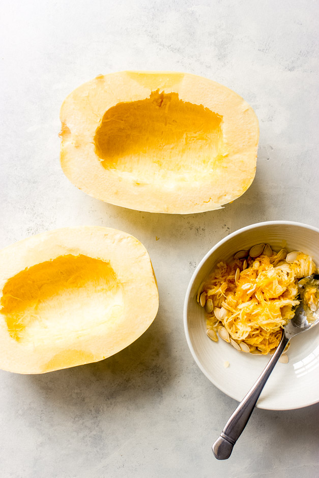 spaghetti squash sliced in half with seeds scooped up in a bowl.