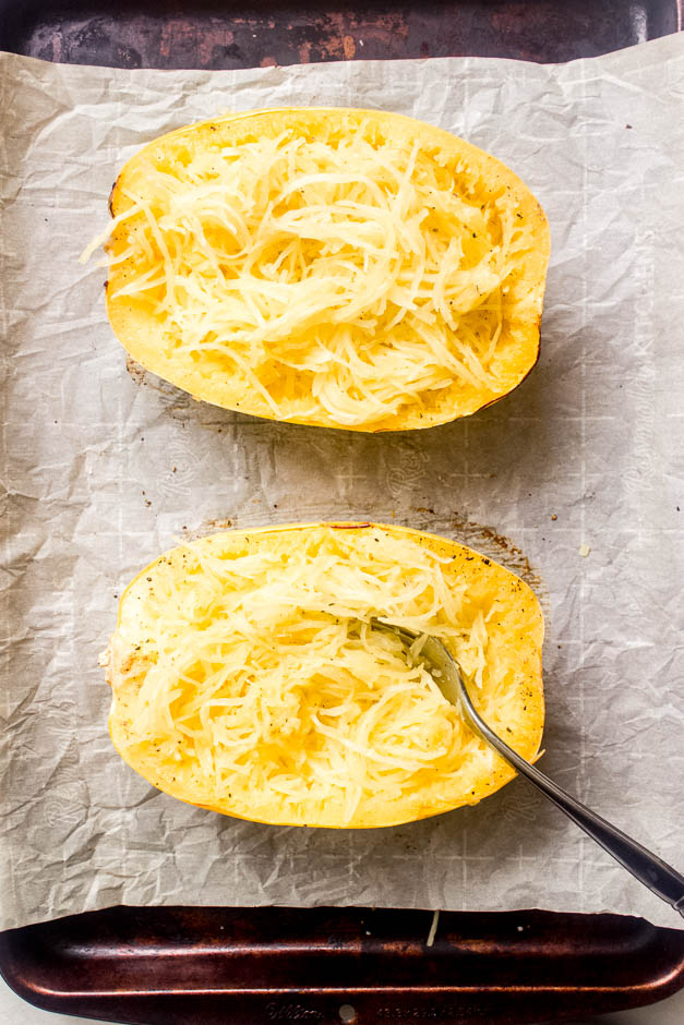 Baked spaghetti squash on a baking sheet with strands scraped up with a fork.