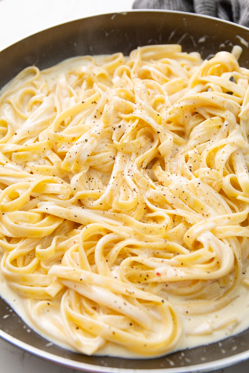 3-ingredient Alfredo sauce in a skillet tossed with cooked fettuccine pasta.