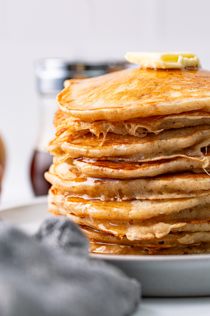 close up of stacked pancakes with syrup on the side.