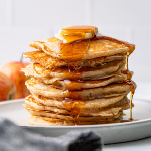 stacked apple cinnamon pancakes with syrup and butter.
