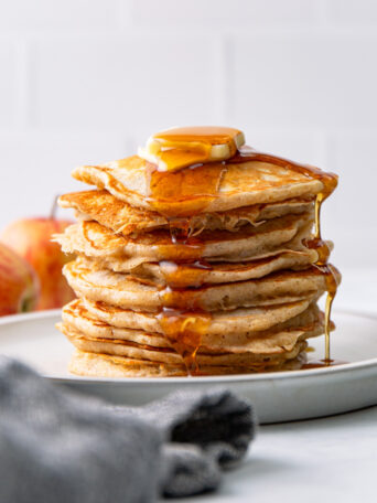 stacked apple cinnamon pancakes with syrup and butter.