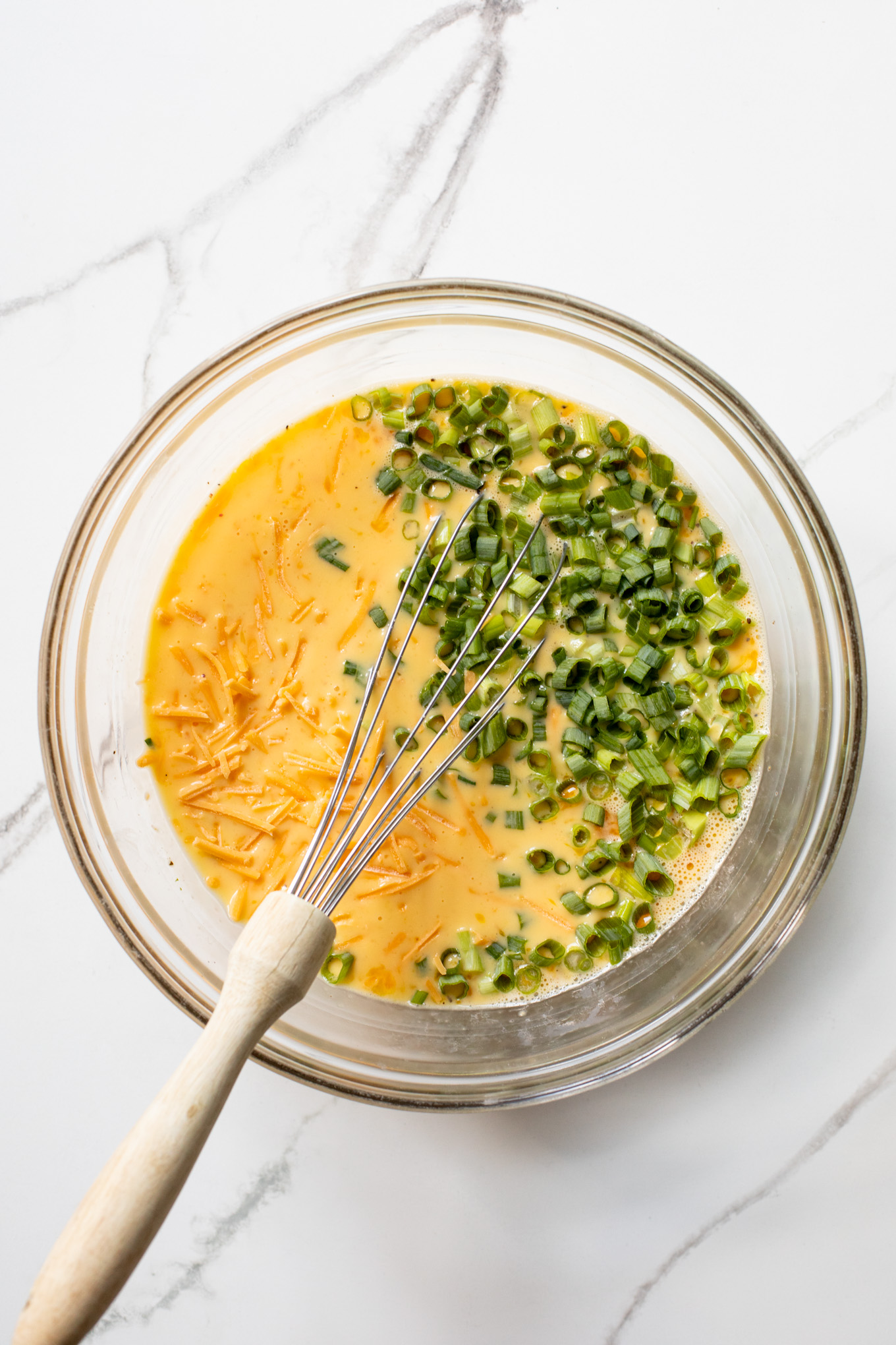 whisked eggs with cheddar cheese and green onions in a bowl.