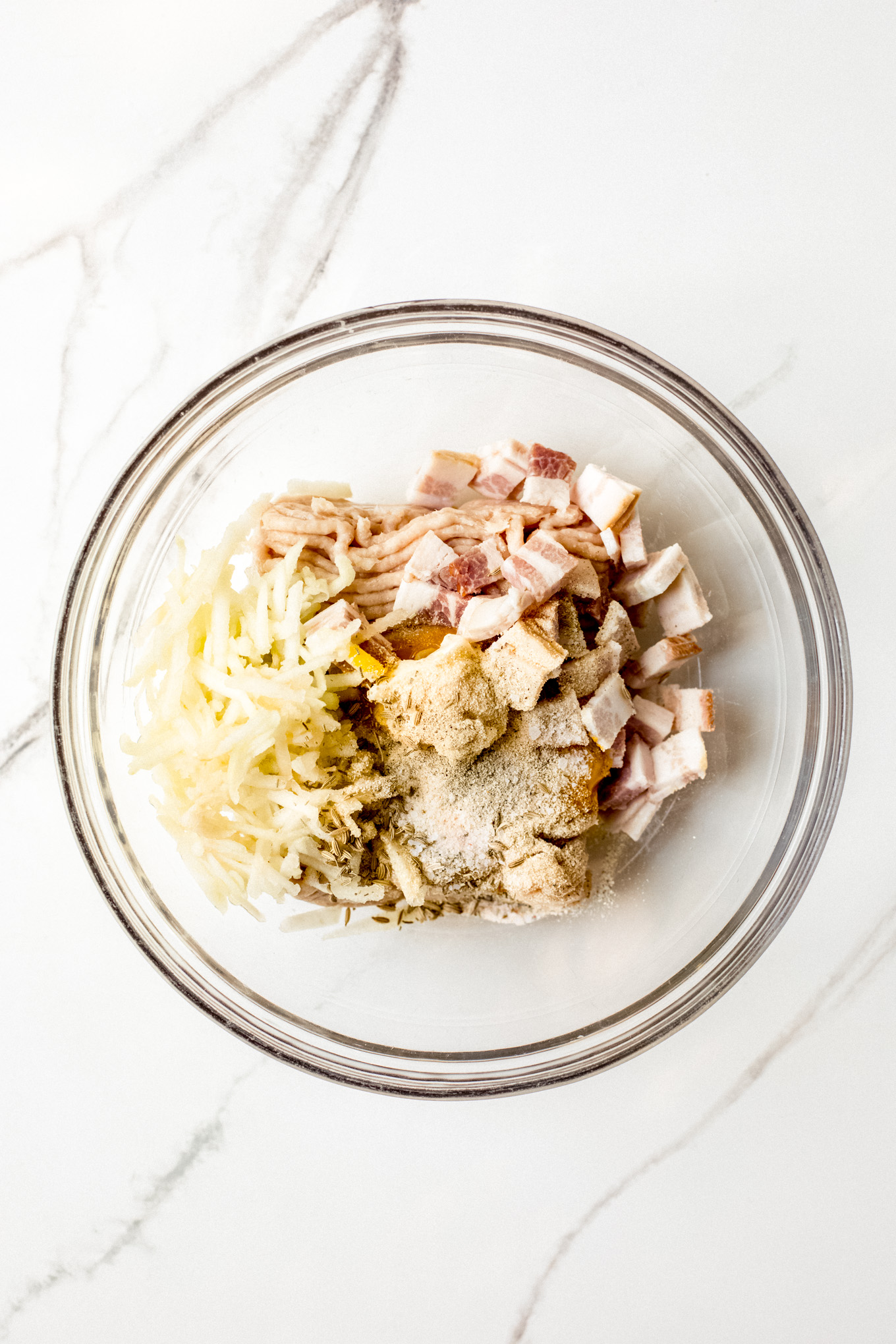 ground chicken, chopped bacon, and shredded apples with spices in a glass bowl.