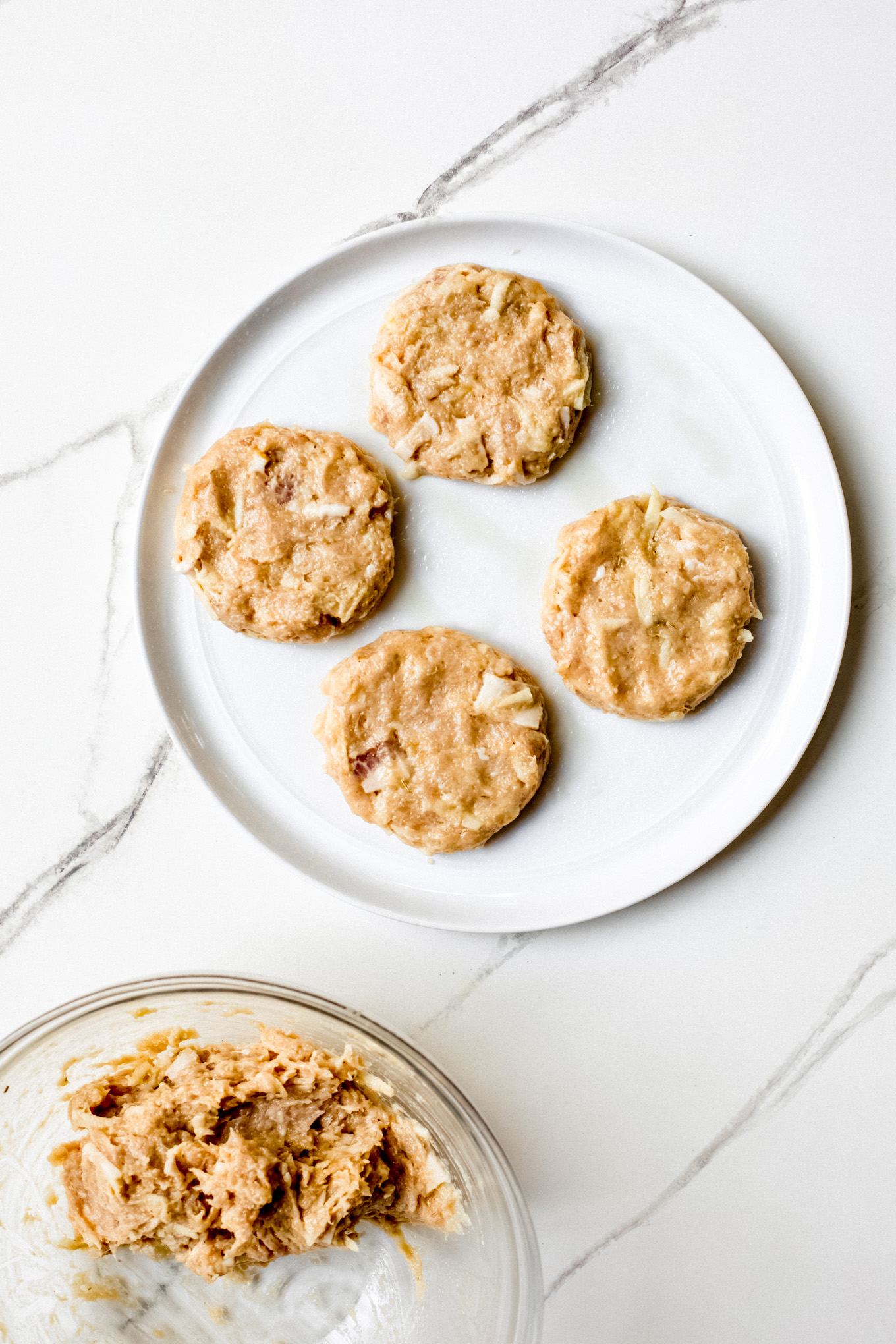 raw chicken patties on a white plate.