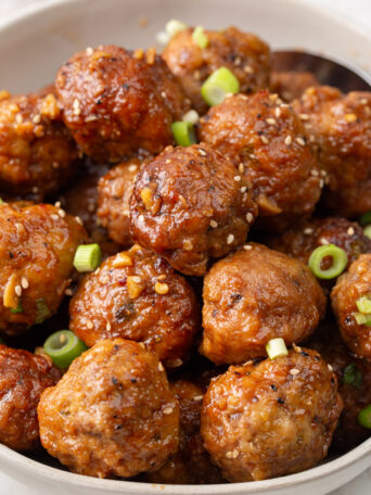 meatballs in a bowl garnished with green onions and sesame seeds.