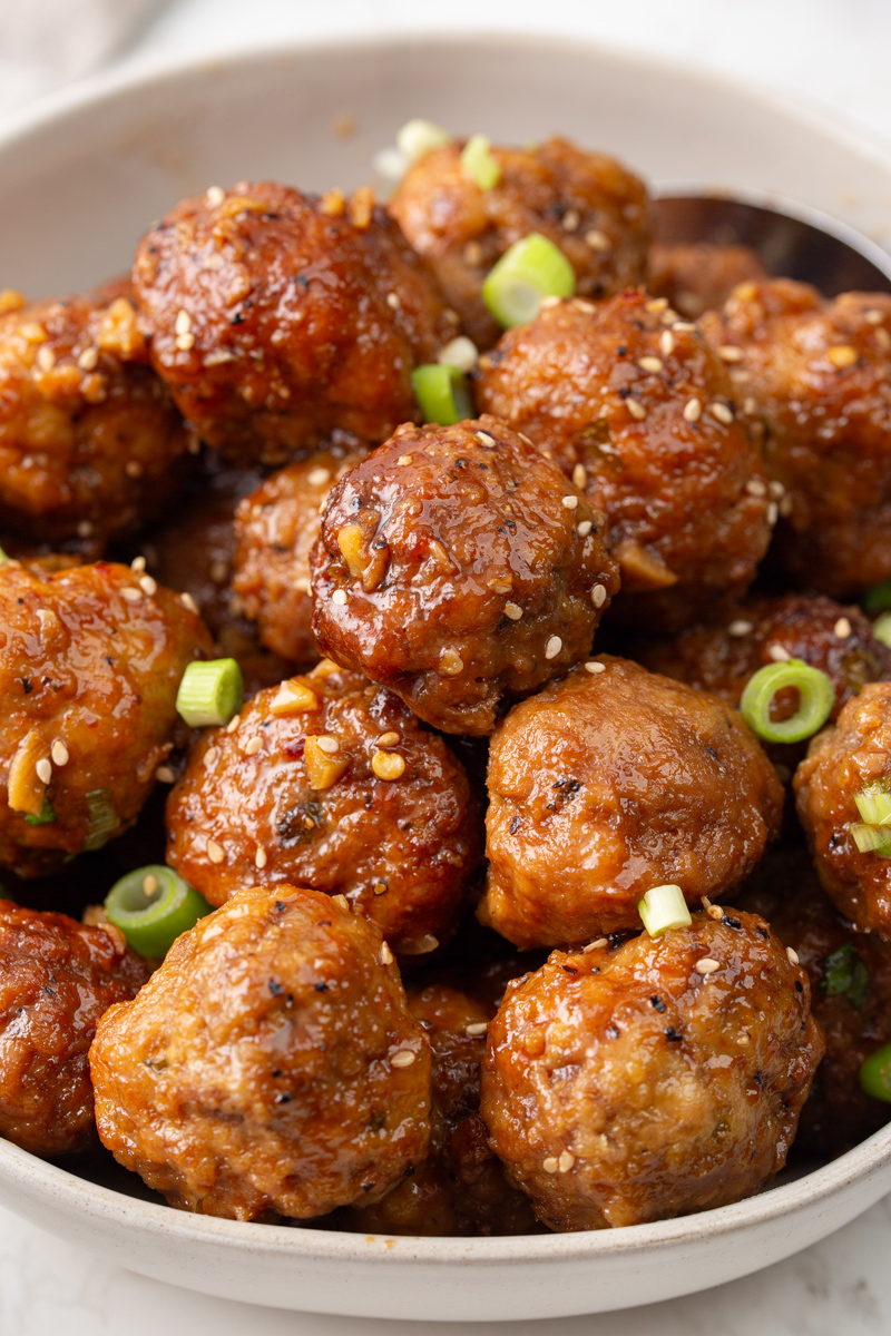 meatballs in a bowl garnished with green onions and sesame seeds.
